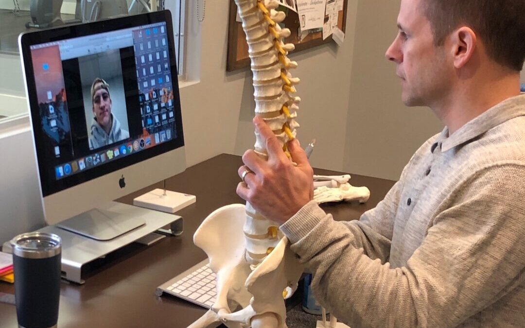 Kregg a physiotherapist sitting at his computer holding a model spine while presenting an online course
